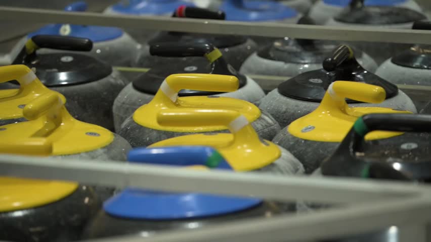 Close view of curling stones arranged on ice rink indoors. Granite stones with colored handles prepared for winter sport training, competition and professional tournament play.