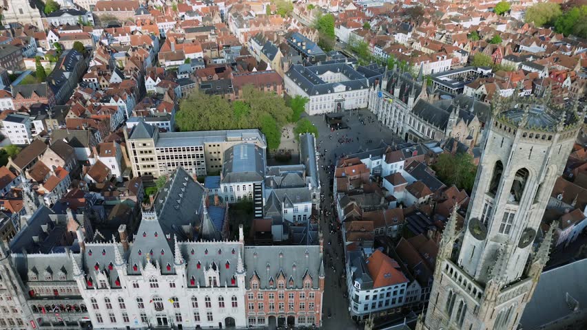 Cinematic aerial shot of the medieval Belfry tower and the historic Markt square in Bruges Belgium featuring traditional architecture and city life in this UNESCO World Heritage site