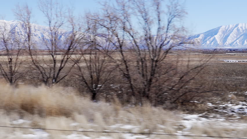 View from moving car looking across field towards snowcapped mountains in Utah Valley.
