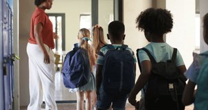 African American teacher gesturing, guiding children down school hall into doorway with backpacks. Educator, students, corridor, lockers, backpack, daylight, lineup - Powered by Shutterstock - Get 15% off with code: PIKWIZARD15