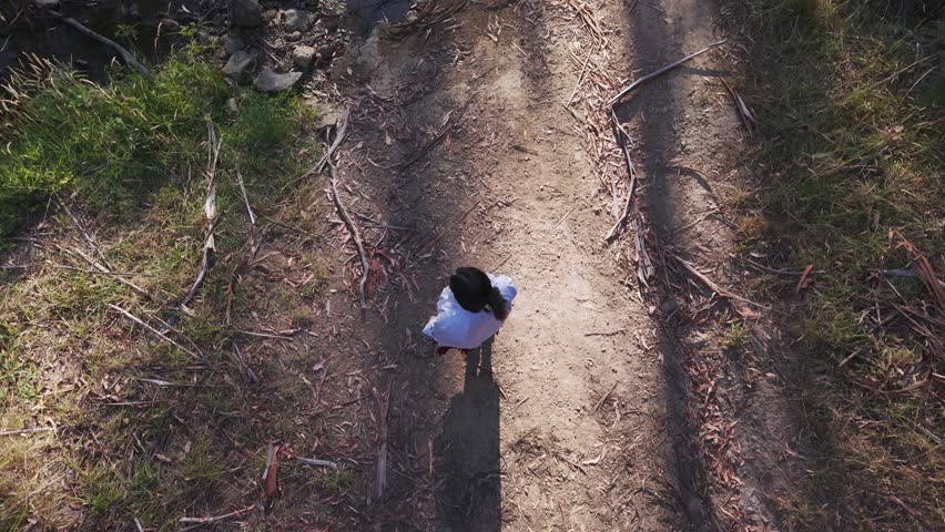 Drone shot of a girl walking over rocks in Warrandyte Park stream, Melbourne. Evening sun casts long shadows, highlighting serene natural beauty. Shot from above, capturing peaceful exploration.