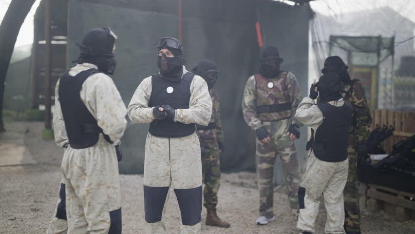 A team of players dressed in camouflage and protective gear prepares for a tactical game. The group discusses strategy before engaging in an exciting outdoor activity.