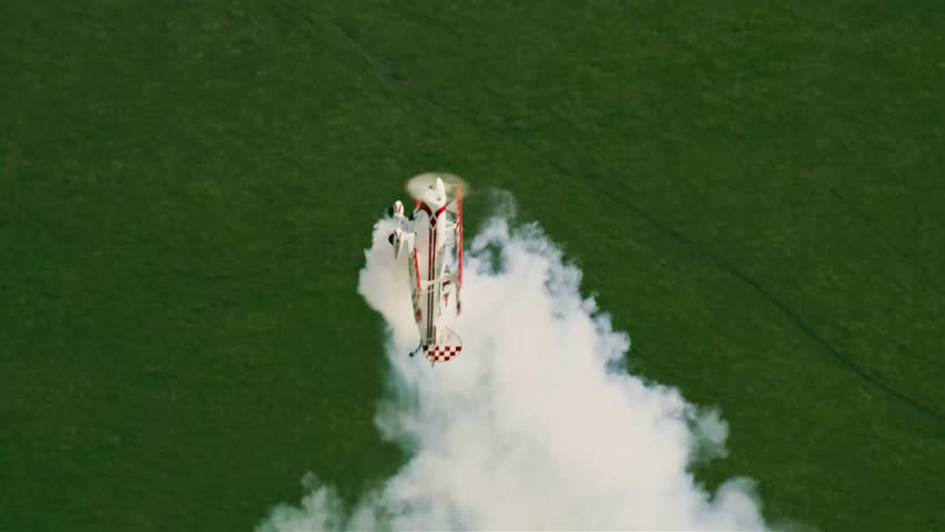 An unmanned aerial vehicle releases a thick plume of white smoke while flying above a vast expanse of green terrain