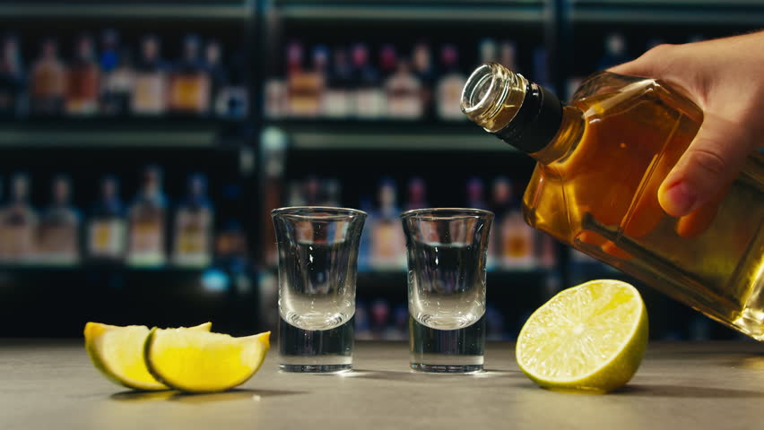 Mexican Tequila Mezcal pouring with lime and salt on a stone table. Strong vodka rum alcoholic drink is poured from a bottle into a shots.
