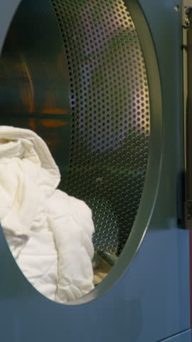Woman in pink sweater loads high-temperature wash blankets into a dryer, showcasing the process of preparing laundry in a modern laundry room setting