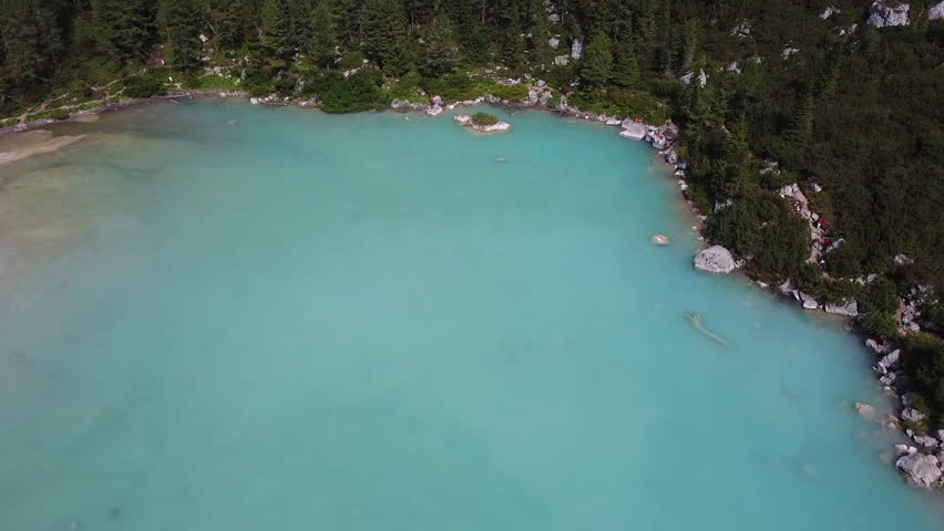 Aerial view of turquoise alpine lake with forested shoreline and rocky edges
