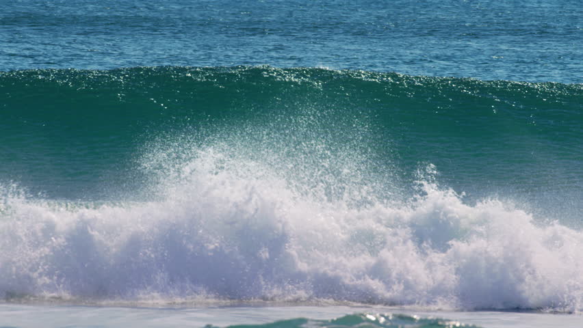 Ocean wave cresting and breaking with white foam under daylight horizon, sparkling glistening mist, slow motion