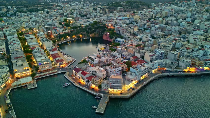 Evening drone view of Agios Nikolaos coastline and city lights in dusk