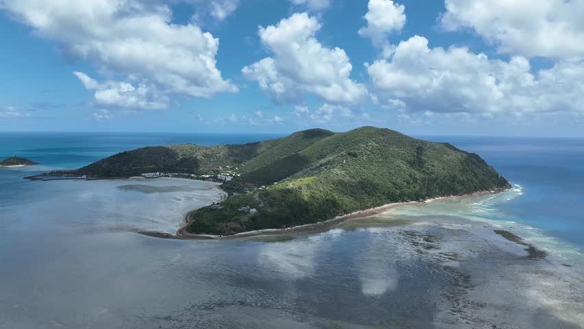 Slow drone tracking shot in daytime, moving sideways along Hayman Island’s coastline to reveal shallow reef flats, sandy shoreline and open ocean, Whitsundays, Queensland, Australia.