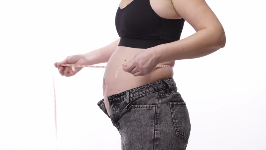 Close-up of female with excess weight measuring waist on white backdrop. Weight loss and healthy lifestyle concept.
