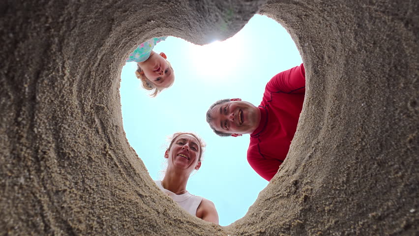 Parents and their little daughter made a hole in the sand in the shape of a heart and took a photo with it. Summer vacation and family time concept