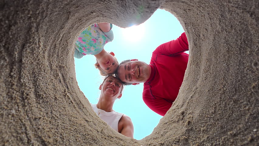 Parents and their little daughter made a hole in the sand in the shape of a heart and took a photo with it. Summer vacation and family time concept