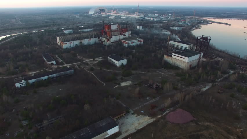 Expansive aerial view of Chernobyl Nuclear Power Plant. Unfinished, abandoned reactor blocks 5 and 6 show decay. New Safe Confinement structure is clearly visible.
