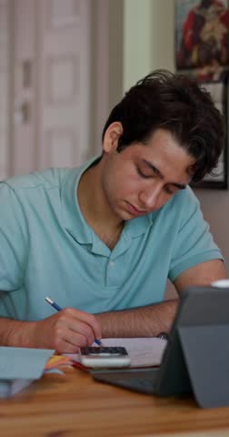College student studies at home, writing notes beside a calculator and tablet while preparing for math and science exams, with subtle lateral movement, vertical format.