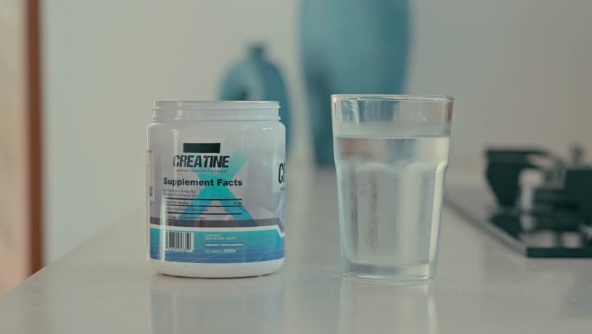 Close-up of a hand adding a scoop of creatine powder to a glass of water and stirring with a spoon to mix the supplement and liquid