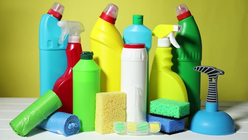 Woman with toilet cleaning products and supplies at white wooden table against yellow background, closeup