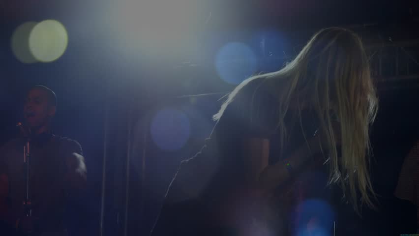 Lead singer onstage grabbing mic moving upright flipping hair backlit lens flares bandmate left. Vocalist, performer, stage, concert, lighting, backlight, rigging