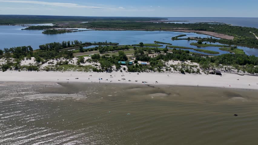 Aerial drone timelapse from far over Lake Winnipeg looking east at Grand Beach, Manitoba. Summer day with people on the beach, sandy shoreline, lagoon, and boreal forest in the background.