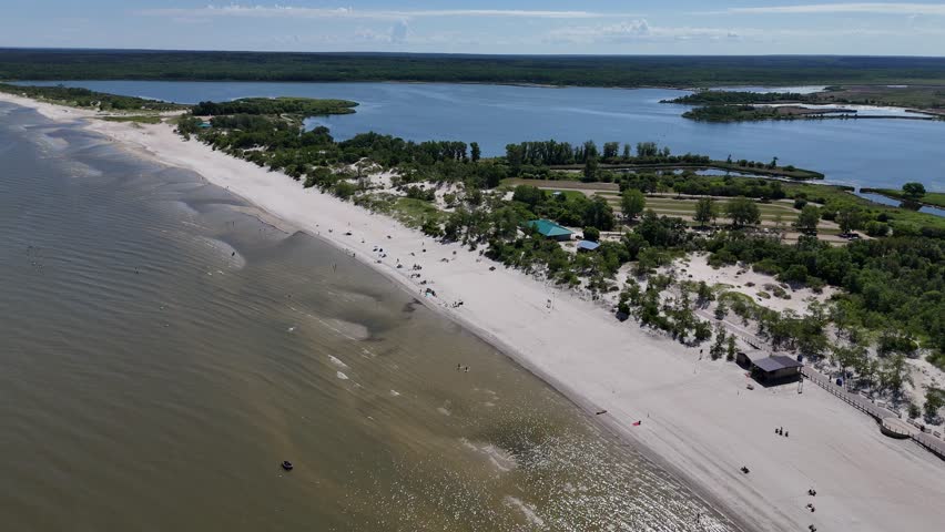 Aerial drone footage from far over Lake Winnipeg looking North at Grand Beach, Manitoba. Summer day with people on the beach, sandy shoreline, lagoon, and boreal forest in the background.