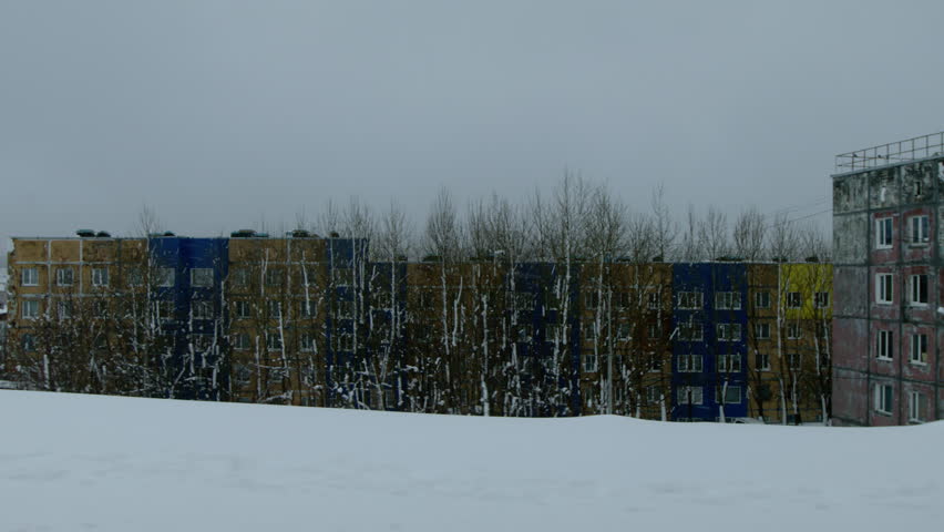 Colorful apartment buildings behind snowy field and bare trees, Kamchatka Russia, slow motion