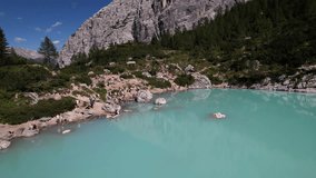 Aerial drone footage flying backwards above the turquoise waters of Lake Sorapis in the Dolomites, revealing the rocky shoreline and alpine landscape. The camera glides smoothly over the lake while distant mountain peaks slowly come into view, showcasing the pristine nature and dramatic scenery of this iconic alpine location. - Powered by Shutterstock - Get 15% off with code: PIKWIZARD15