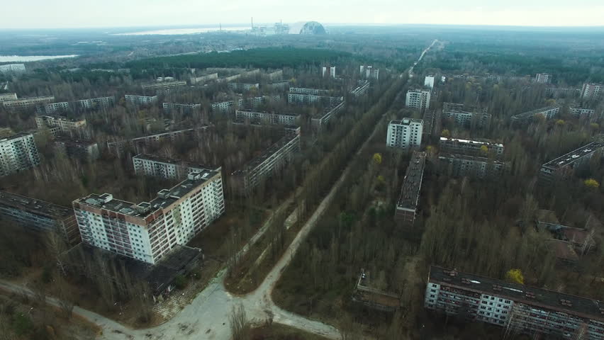 Drone footage of Pripyat, Ukraine, an abandoned city near Chernobyl Nuclear Power Plant. Residential blocks and roads are overgrown by dense forests. Distant Chernobyl New Safe Confinement structure v
