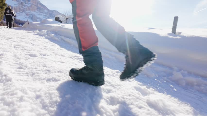 Slow motion close up of hiking boots walking through fresh snow on mountain trail. Winter adventure, outdoor lifestyle and trekking concept in alpine landscape.