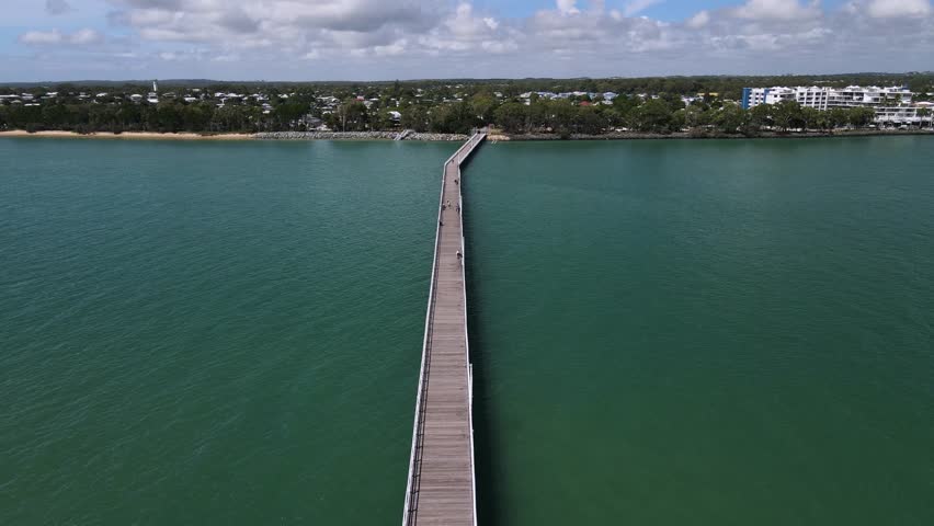 Aerial view of the historic Urangan Pier and foreshore located in the coastal town of Hervey Bay Queensland Australia. Moving drone view