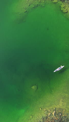 Vertical View Of A Canoe Boat Sailing In Green Lake Lagoon. Aerial Ascending Shot