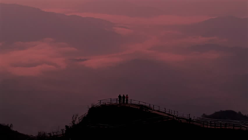 Majestic mountain landscape and sea of fog at dawn with silhouettes of people.