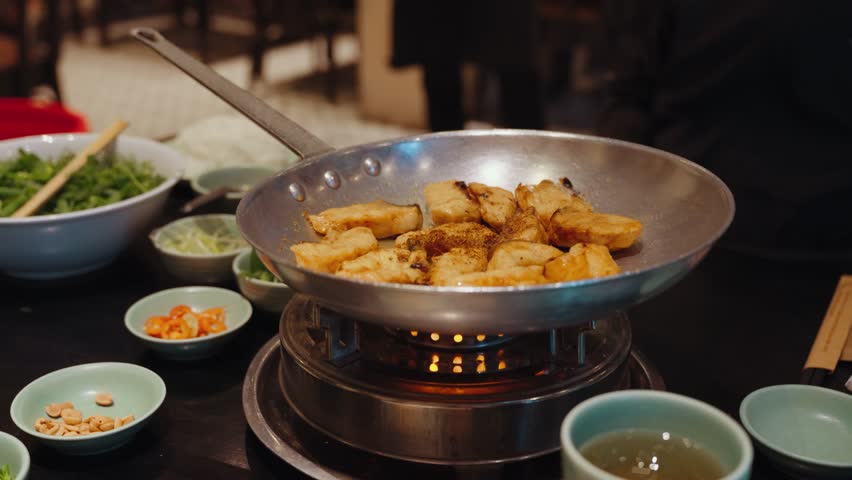 Chefs prepare traditional cha ca fish with turmeric and fresh herbs at Cha Ca Thang Long restaurant in Hanoi, Vietnam, showcasing a classic northern Vietnamese culinary experience.