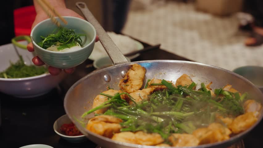 Chefs prepare traditional cha ca fish with turmeric and fresh herbs at Cha Ca Thang Long restaurant in Hanoi, Vietnam, showcasing a classic northern Vietnamese culinary experience.