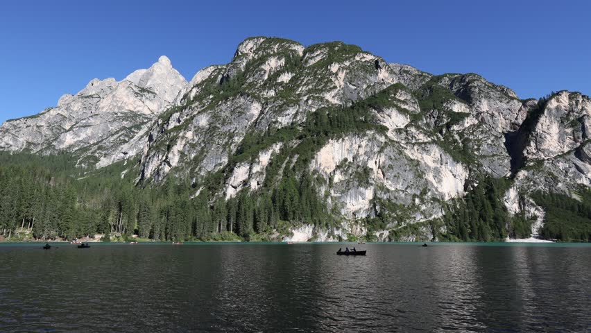 Breathtaking beauty of Pragser Wildsee, calm alpine lake Braies with emerald waters nestled amidst Dolomite mountains with towering rocky peaks on sunny summer day, Italy