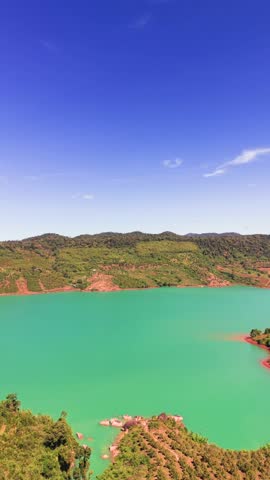 The lake in Lam Dong, Vietnam, reflects the blue sky. The green hills surround the water, creating a natural area that shows the region