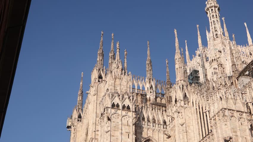 Stunning low angle shot looking up at the numerous marble spires of the Milan Duomo against a clear sky. Iconic gothic landmark silhouette