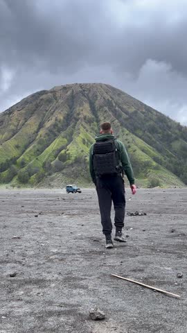 Traveler walking across Sea of Sand toward Mount Batok near Mount Bromo in East Java, Indonesia. Dramatic volcanic landscape in Southeast Asia. Concepts of travel, nature, and adventure.