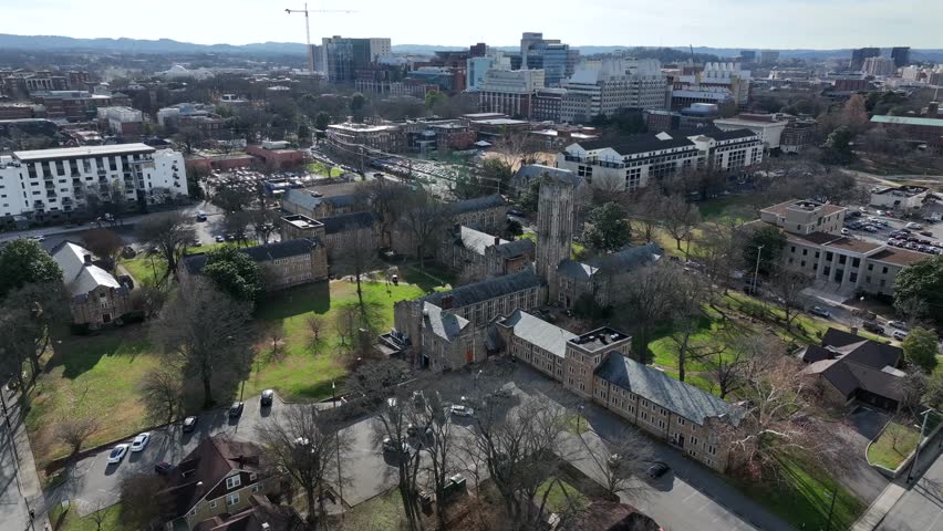 Aerial view of Nashville, Tennessee with university campus buildings, green lawns, historic stone architecture and expanding downtown skyline under clear daylight. Wide shot. Approaching shoty