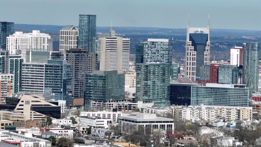 Aerial view of Nashville Tennessee skyline with modern glass skyscrapers, high rise office towers and vibrant downtown architecture under clear blue sky daylight. Wide shot.