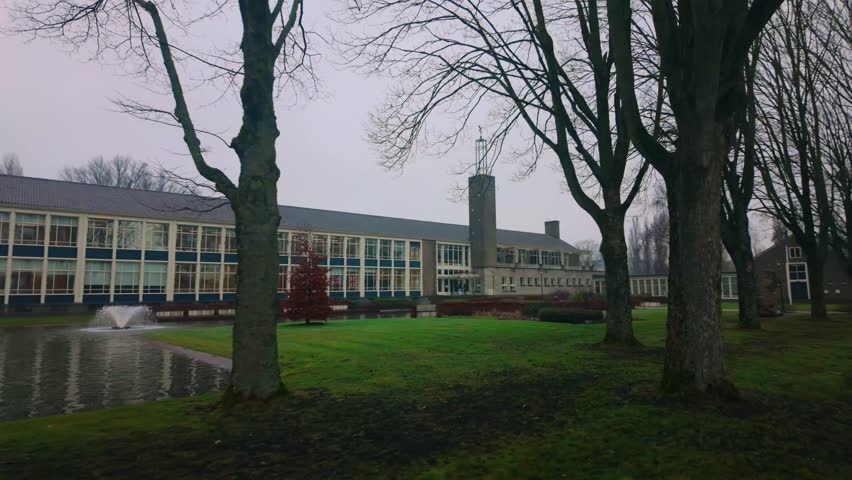 Wide shot of SGA educational facility in Arnhem Netherlands with bare trees and fountain in front, showcasing the modernist facade and surrounding green space in winter.