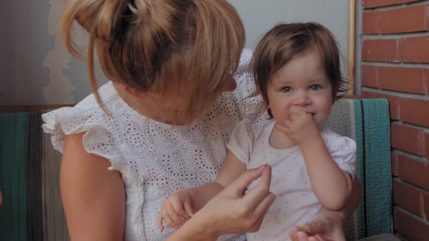Young caring mother holding her little daughter on her lap, playing and smiling together outdoors