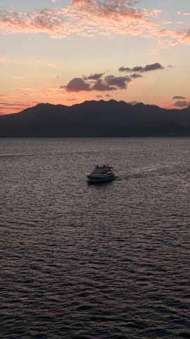 Golden light fades over distant mountains. Lone boat glides across calm waters. Soft waves ripple beneath twilight hues. Serene moment invites quiet reflection