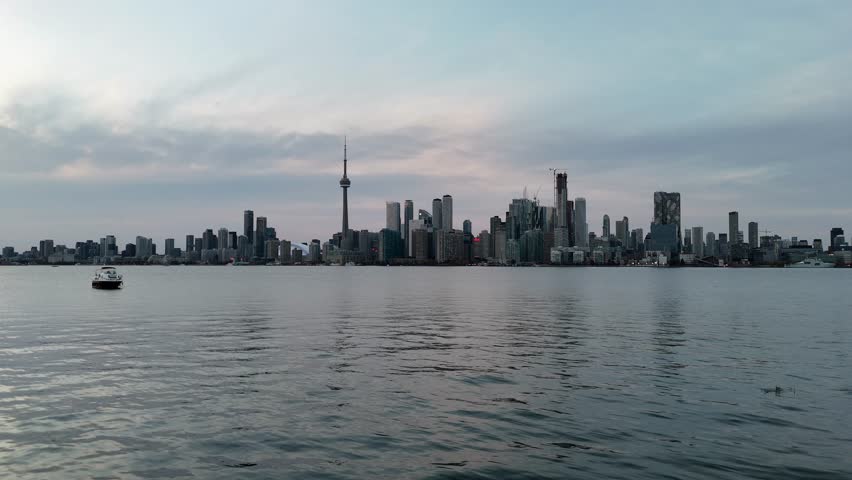 Serene Toronto city skyline at dusk with a boat on calm lake waters, showcasing urban architecture and peaceful atmosphere
