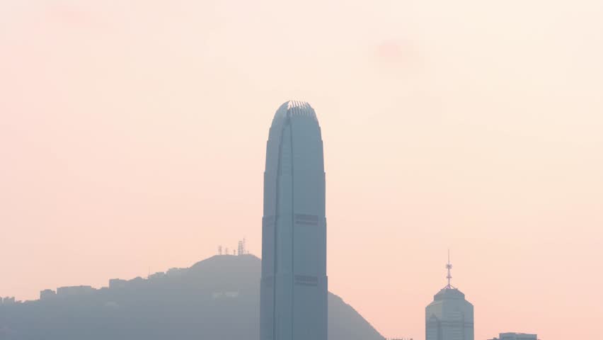 Panoramic view of the Two International Finance Center skyscraper from Victoria Harbour in downtown Hong Kong during sunset, featuring warm light over the iconic skyline.