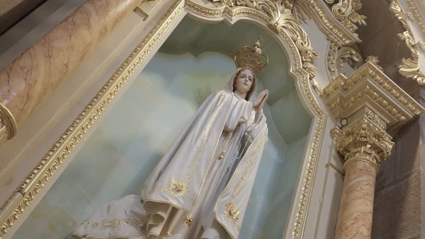 Low angle view of crowned Virgin Mary statue inside decorative altar niche with gilded frame column and painted sky background in catholic church