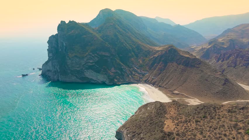 Aerial view of the turquoise ocean and white sand coastline surrounded by high rocky cliffs at Afoul Beach, Salalah, Oman.