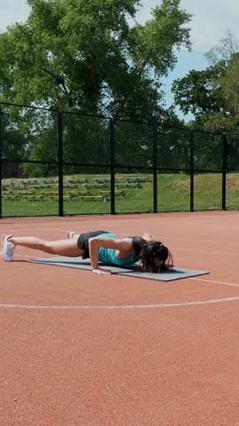 Fitness woman in sportswear doing various exercises on sports mat, on an orange basketball field with white markings, at the stadium. Outdoor sports. online training. summer day.