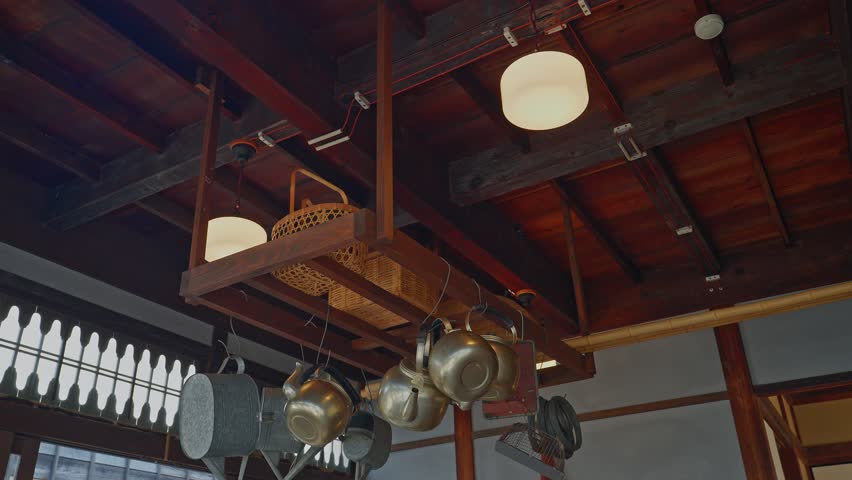 A cinematic low-angle shot of overhead storage in a historic Japanese merchant house. Features brass kettles and bamboo baskets hanging from dark wooden beams at Edo-Tokyo Open Air Architectural Museu