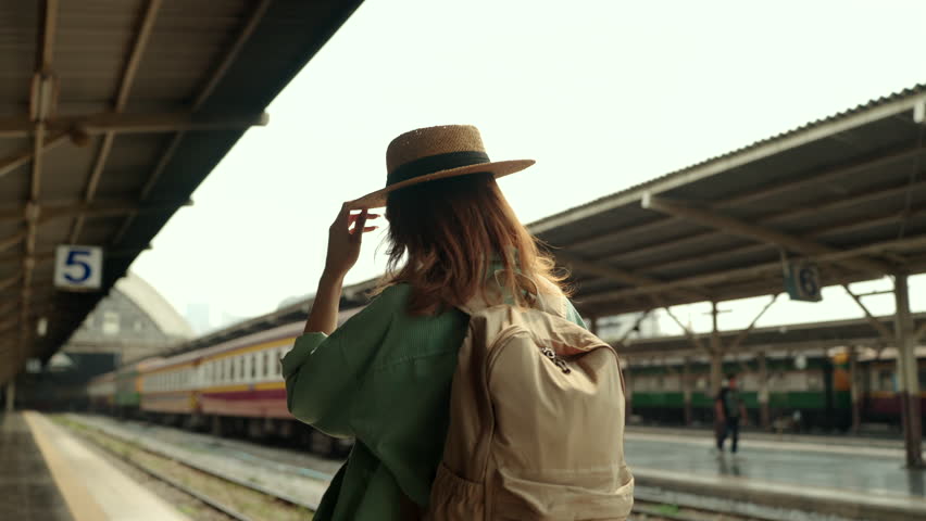 Back view of young beautiful woman solo traveler walking along a train platform during summer vacation, travel insurance for safe travel lifestyle.
