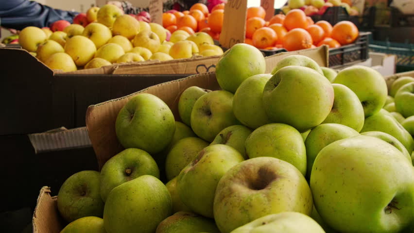 Close-up view of green apples piled high at outdoor farmers market. People buying fresh fruits at local market