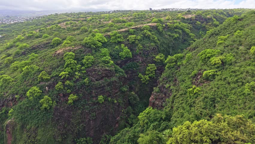 Wide drone ascension over Ravine Bernica with downward tilt revealing river gorge, Saint-Paul, Reunion Island